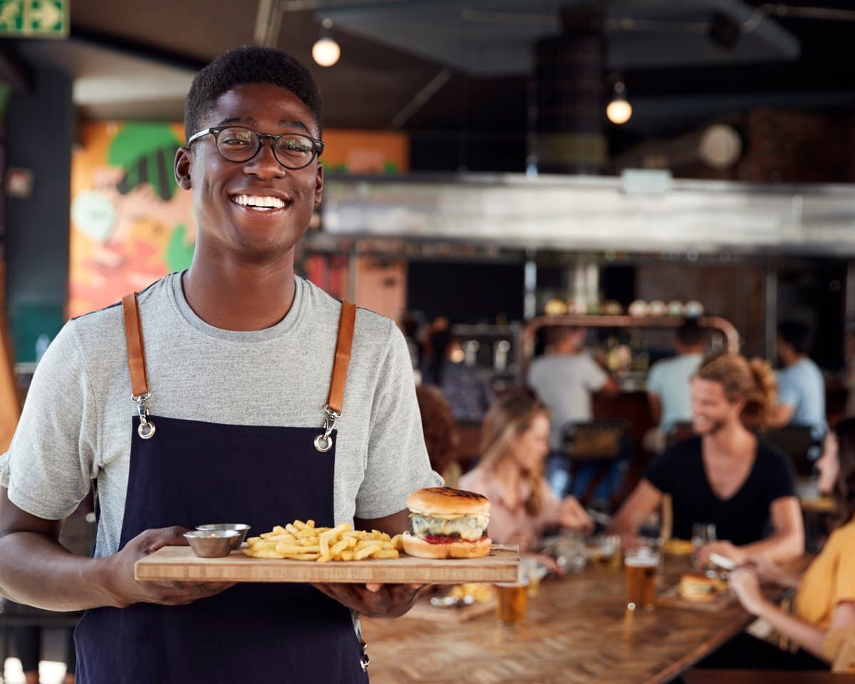 A small-business owner smiling in their restaurant, serving a fresh plate